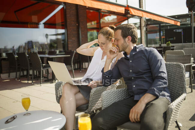 Homme et femme utilisant un ordinateur portable assis au bar — Photo de stock