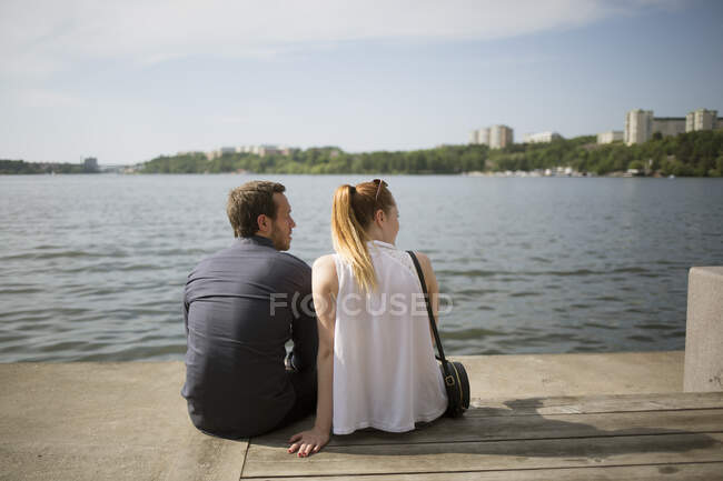 Couple assis côte à côte au bord de l'eau — Photo de stock