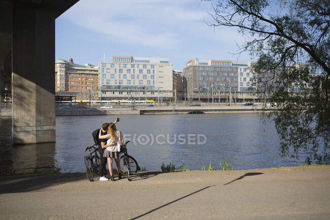 Couple with bicycles taking selfie by waterfront — Stock Photo