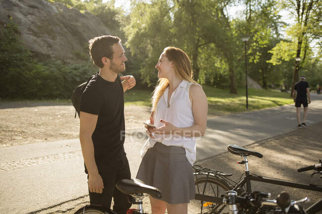 Jeune homme et femme avec des vélos dans le parc — Photo de stock