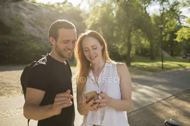 Jovem e mulher usando smartphone no parque — Fotografia de Stock