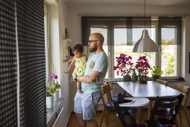 Man holding daughter while looking out window — Stock Photo
