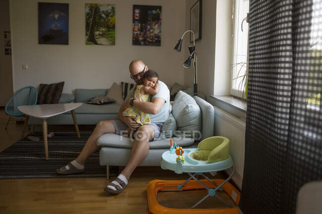 Hombre abrazando a su hija mientras está sentado en el sofá - foto de stock