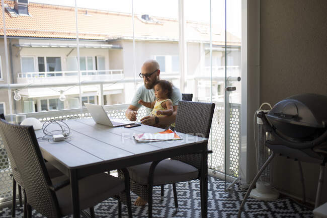 Mann arbeitet von zu Hause aus, während er seine Tochter hält — Stockfoto