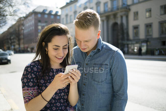 Mujer mostrando el hombre su teléfono inteligente en la calle - foto de stock