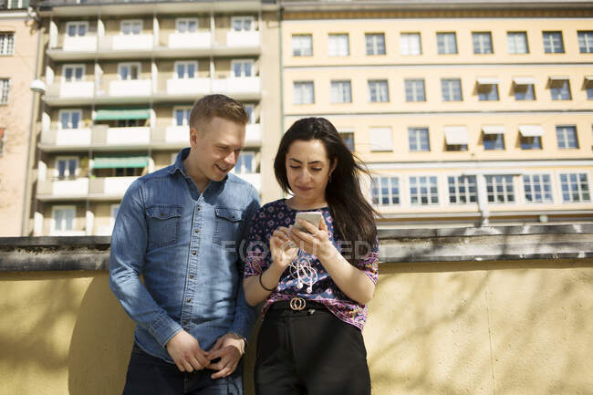 Mujer mostrando hombre su teléfono inteligente en el balcón - foto de stock