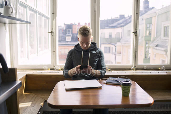 Молодий чоловік зі смартфоном за столом в офісній кімнаті відпочинку — стокове фото