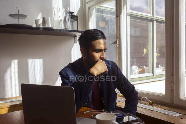 Hombre con portátil pensando por ventana - foto de stock