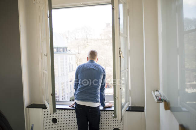 Jeune homme par fenêtre dans le bureau — Photo de stock