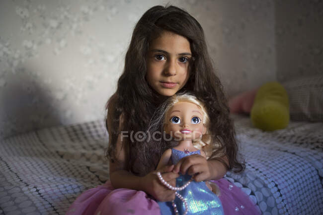 Chica sentada con su muñeca en la cama - foto de stock
