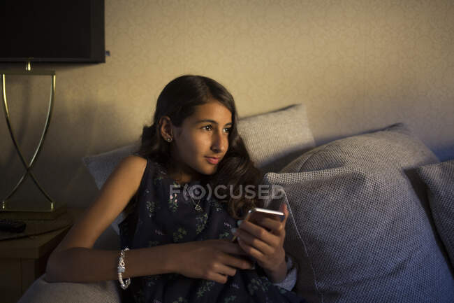 Chica con teléfono inteligente sentado en el sofá - foto de stock