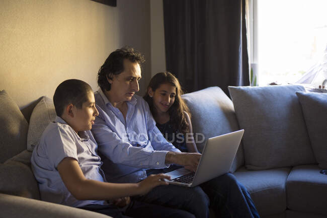 Чоловік з ноутбуком сидить з дітьми на дивані. — стокове фото