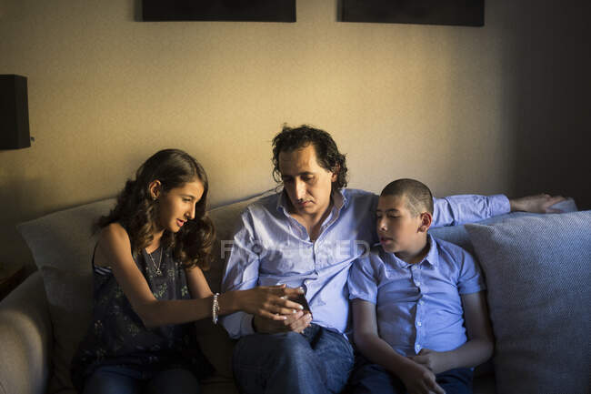 Мужчина со смартфоном сидит со своими детьми на диване — стоковое фото