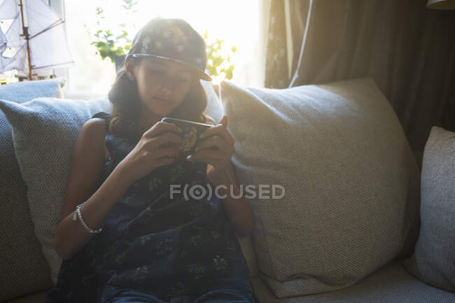 Menina usando smartphone enquanto sentado no sofá — Fotografia de Stock