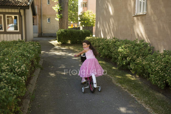 Girl riding bicycle with training wheels — Stock Photo