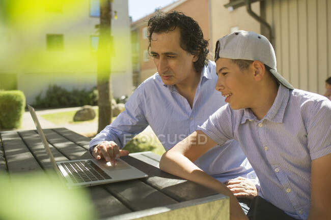 Человек помогает сыну учиться за открытым столом — стоковое фото