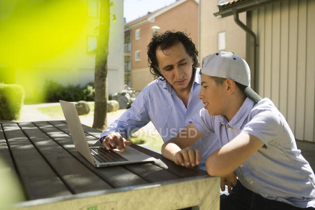 Человек помогает сыну учиться за открытым столом — стоковое фото