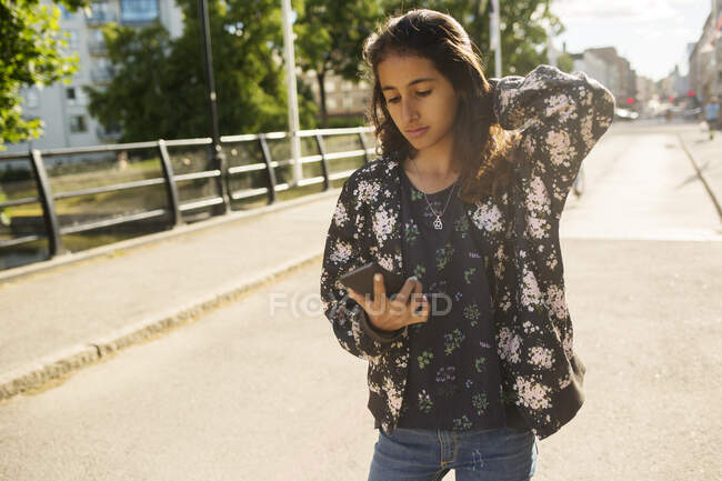 Девушка держит смартфон во время прогулки по мосту — стоковое фото