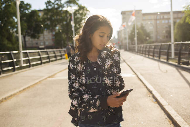 Ragazza che tiene smartphone mentre cammina sul ponte — Foto stock