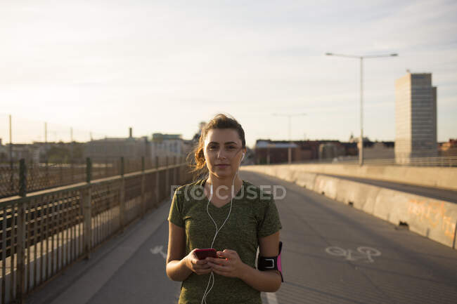 Young woman listening to music on bridge — Stock Photo