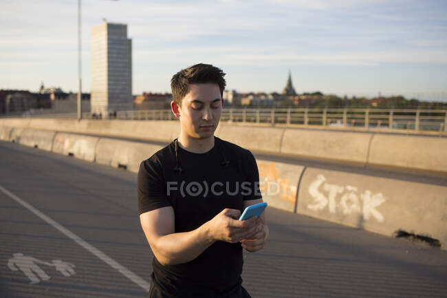 Молодой человек использует смартфон на мосту — стоковое фото