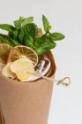 Glass of refreshing drink with mint and citrus slices wrapped in craft paper — Stock Photo