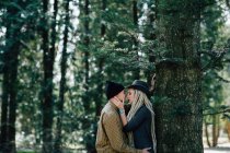 Stylish young couple leaning on tree trunk in woods — Stock Photo