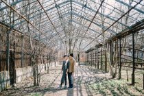 Jeune couple marchant dans une serre abandonnée avec des arbres nus — Photo de stock