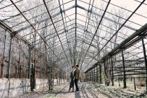 Young couple posing at abandoned greenhouse with bare trees — Stock Photo