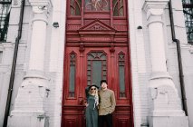 Elegante pareja posando en la puerta roja ornamentada - foto de stock