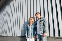 Jeune couple adulte portant des vêtements décontractés debout près du mur — Photo de stock