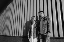 Jovem casal adulto vestindo roupas casuais em pé perto da parede, preto e branco — Fotografia de Stock