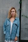 Junge erwachsene Frau in Freizeitkleidung vor grauer Wand und blickt in die Kamera — Stockfoto