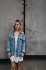 Joven mujer adulta en ropa casual contra la pared gris mirando a la cámara - foto de stock