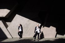 Ganzkörperaufnahme von zwei Frauen in klassischen Anzügen, die im Freien gegen eine geometrische Betonwand posieren — Stockfoto