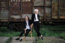 Tiro de comprimento total de duas mulheres posando na estação ferroviária, um sentado na cadeira e outro de pé perto — Fotografia de Stock