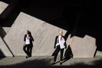 Tiro de comprimento total de duas mulheres em ternos clássicos posando contra parede de concreto geométrico ao ar livre — Fotografia de Stock