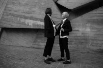 Полный снимок женщины, связывающей свою подругу с геометрической бетонной стеной на открытом воздухе — стоковое фото