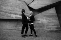 Полный снимок женщины, связывающей свою подругу с геометрической бетонной стеной на открытом воздухе — стоковое фото