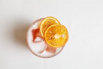 Top view of cold cocktail with ice cubes and dried orange slices — Stock Photo