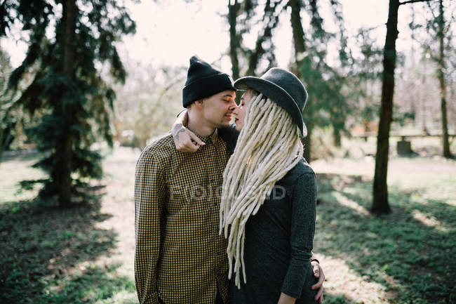 Стильная молодая пара, обнимающая и трящая носы в солнечном парке — стоковое фото