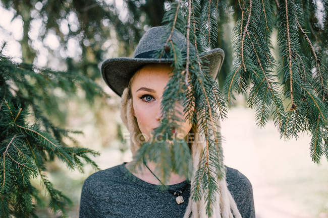 Portrait of stylish woman with dreadlocks under coniferous tree — Stock Photo