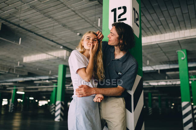 Casal jovem colagem por coluna no estacionamento — Fotografia de Stock