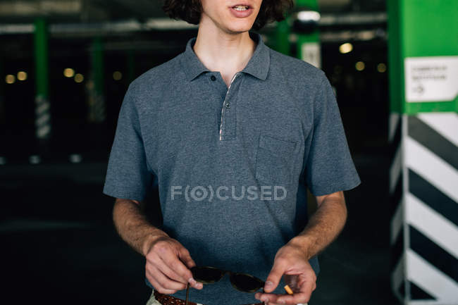 Midsection of young man holding cigarette and sunglasses at parking — Stock Photo