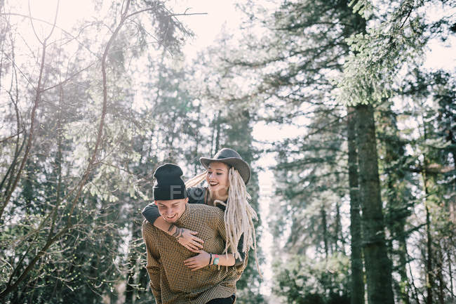 Elegante ragazza con dreadlocks abbracciando ragazzo da dietro alla scena della foresta — Foto stock