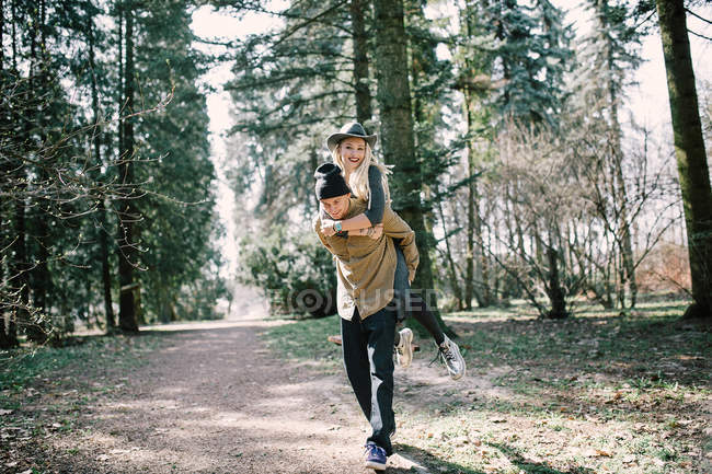Fröhliches Mädchen mit blonden Dreadlocks, das in der Natur auf dem Rücken seines Freundes reitet — Stockfoto