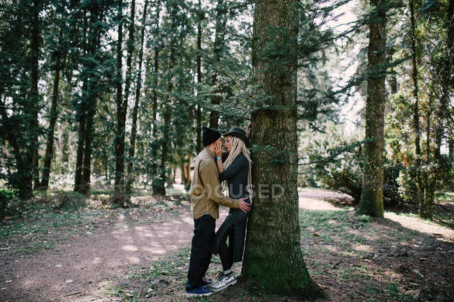 Young couple kissing by tall tree trunk at park\ — Fotografia de Stock