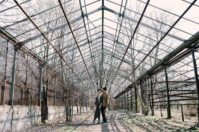 Junges Paar posiert vor verlassenem Gewächshaus mit kahlen Bäumen — Stockfoto