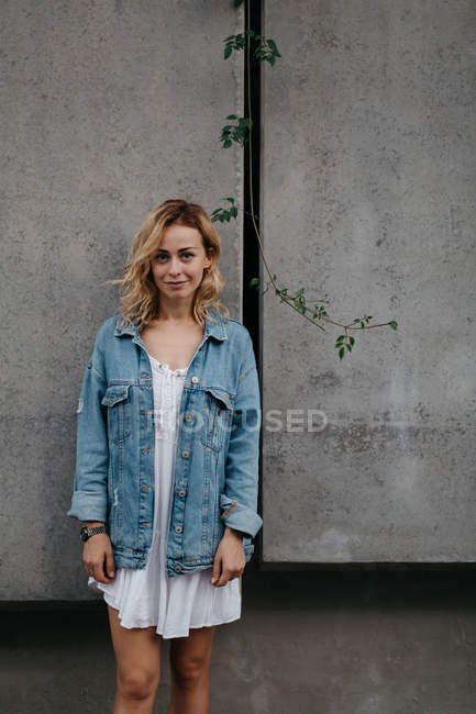 Junge erwachsene Frau in Freizeitkleidung vor grauer Wand und blickt in die Kamera — Stockfoto