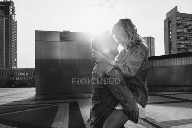 Young adult couple hugging on city street against sky, black and white — Stock Photo